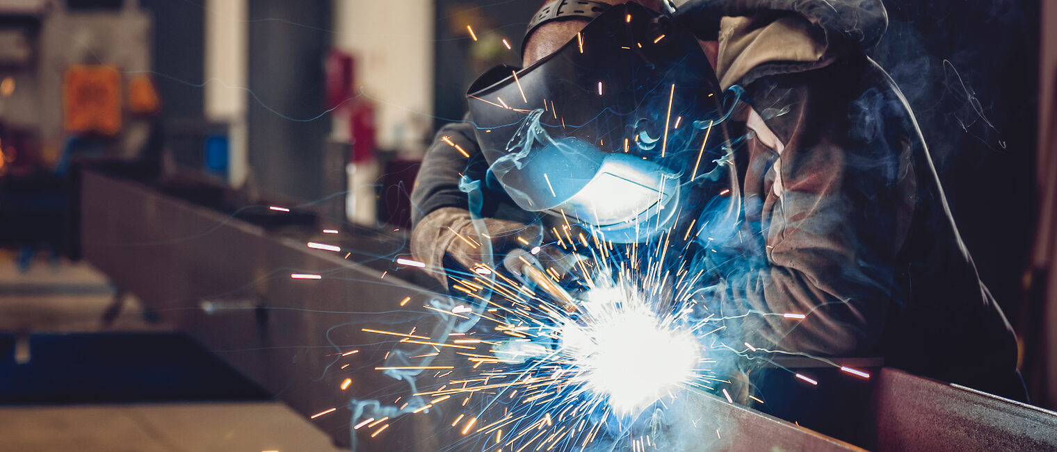 Industrial Welder With Torch and Protective Helmet in big hall welding metal profiles Schlagwort(e): mig welding