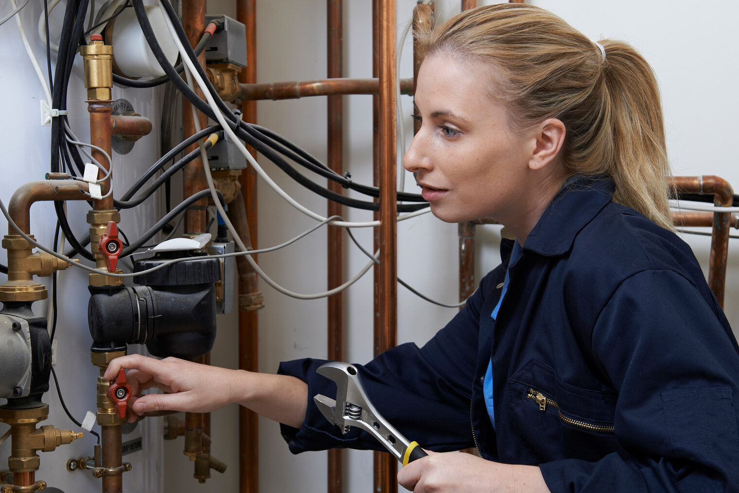 Frauen. Handwerk. Südwestfalen. Eine Handwerkerin repariert eine Heizungsanlage in einem Keller.