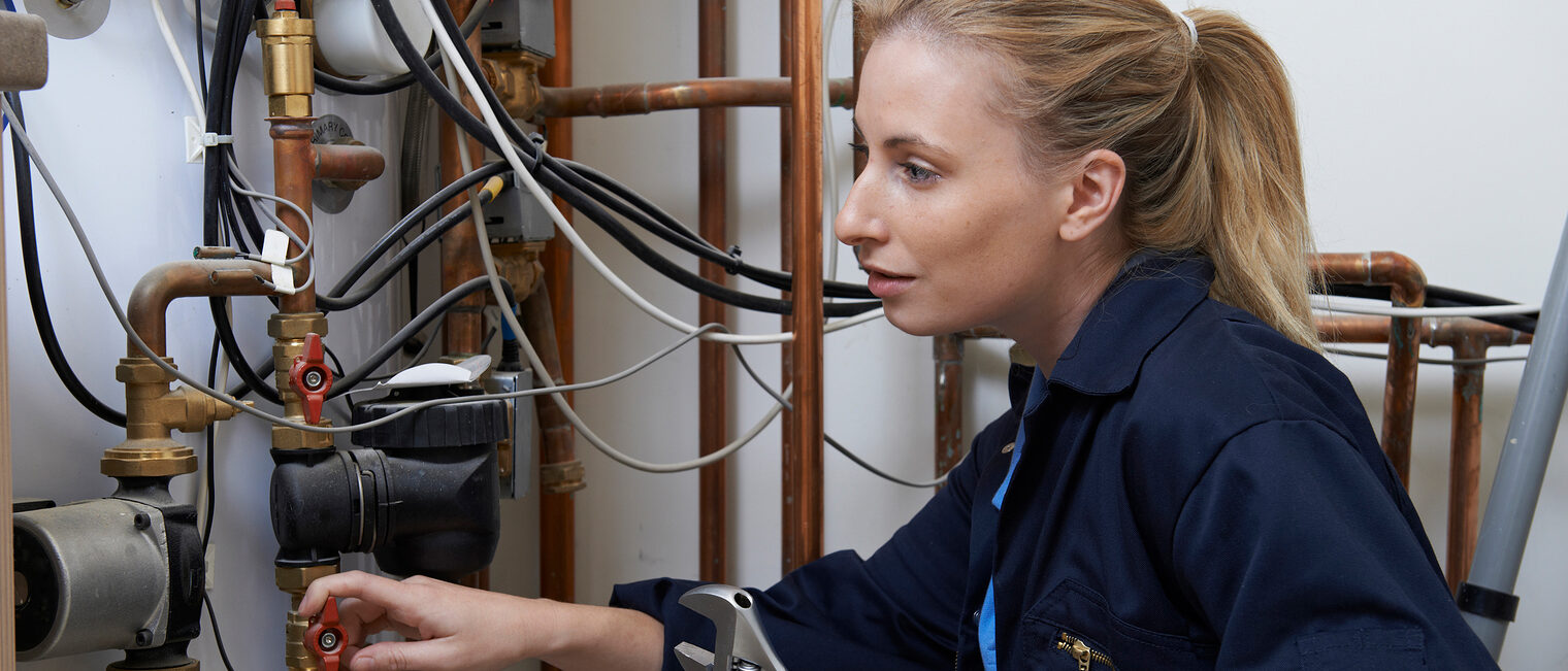 Frauen. Handwerk. Südwestfalen. Eine Handwerkerin repariert eine Heizungsanlage in einem Keller.